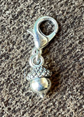A small silver acorn charm with a lobster clasp, resting on a textured gray fabric background.